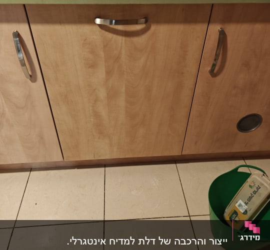 ארון מטבח עם ידיות מתכת ודלי ירוק על הרצפה